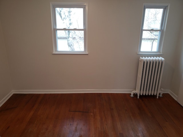 empty room with baseboards, dark wood finished floors, and radiator