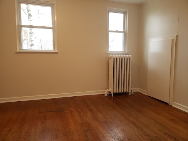 empty room with baseboards, dark wood-style floors, and radiator heating unit