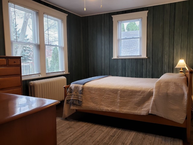 bedroom with radiator, wooden walls, and wood finished floors