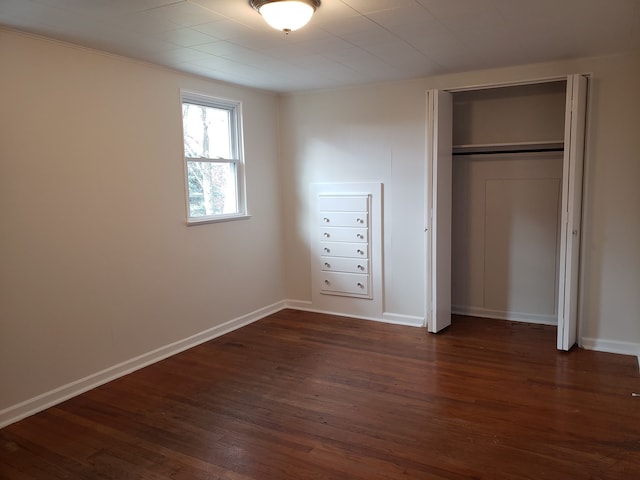 unfurnished bedroom featuring a closet, dark wood-style floors, and baseboards