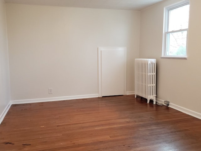 empty room featuring baseboards, wood finished floors, and radiator
