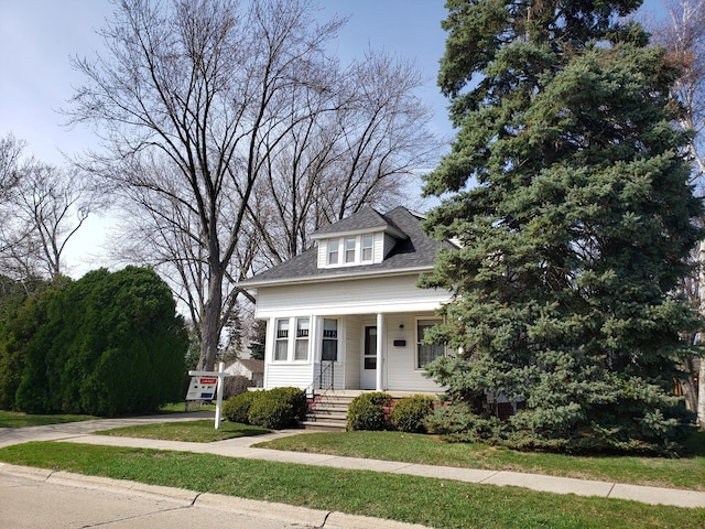 bungalow-style home featuring covered porch, a front yard, and roof with shingles