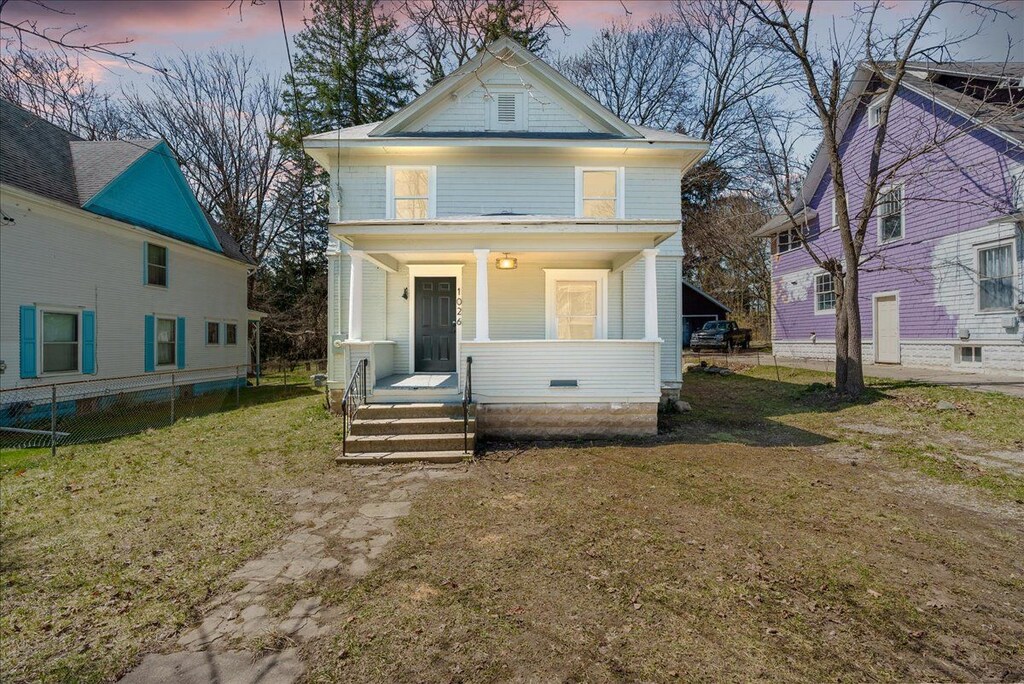 1026 S Jackson St, Jackson, MI 49203 - american foursquare style home featuring a porch, fence, and a front lawn
