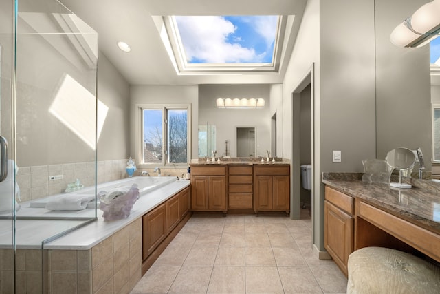 bathroom featuring vanity, tile patterned floors, a tray ceiling, a skylight, and a garden tub