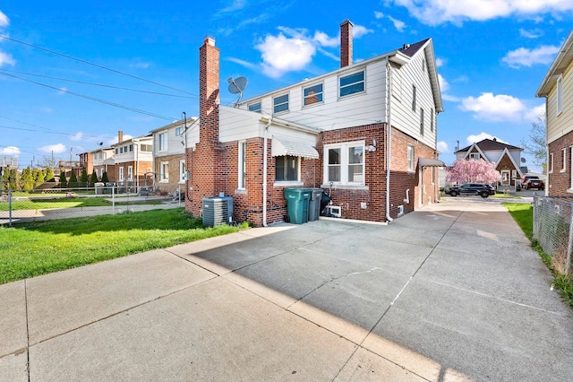 back of house with a residential view, cooling unit, a lawn, brick siding, and fence