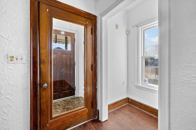 interior space featuring dark wood-style floors, baseboards, a wealth of natural light, and a textured wall