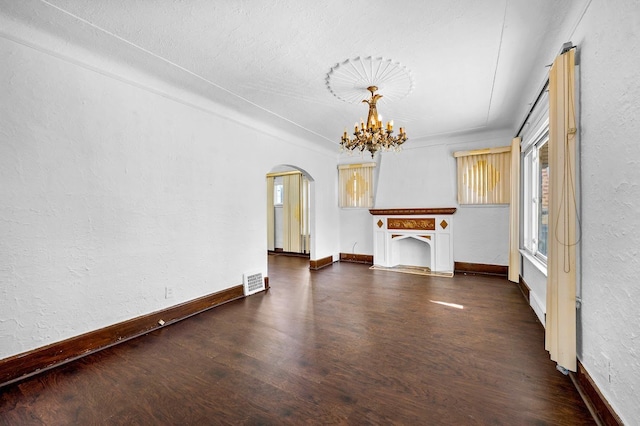 unfurnished dining area with arched walkways, a textured wall, wood finished floors, and a healthy amount of sunlight