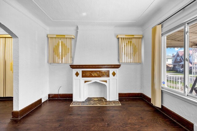 unfurnished living room featuring dark wood-style floors, baseboards, and arched walkways