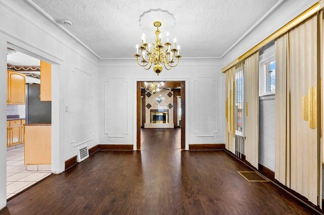 unfurnished dining area with a textured ceiling, a notable chandelier, wood finished floors, and visible vents