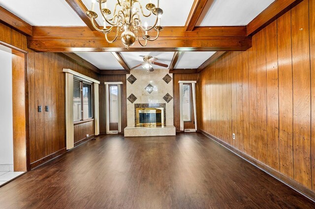 unfurnished living room with wood walls, a premium fireplace, beam ceiling, wood finished floors, and ceiling fan with notable chandelier