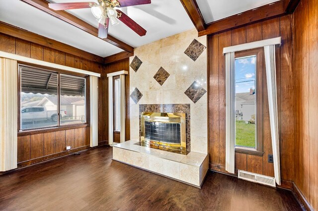 unfurnished living room with beam ceiling, dark wood-type flooring, visible vents, and wood walls