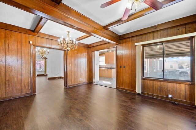unfurnished room featuring beam ceiling, wood walls, ceiling fan with notable chandelier, and dark wood-style floors