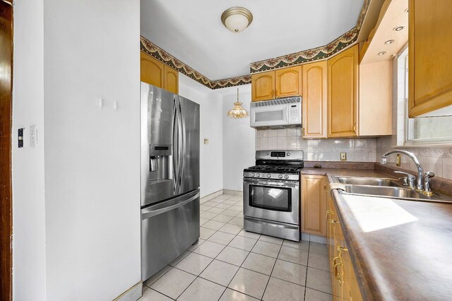 kitchen with light tile patterned floors, stainless steel appliances, decorative backsplash, and a sink