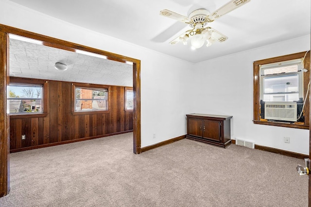carpeted empty room featuring baseboards, visible vents, a ceiling fan, and wood walls