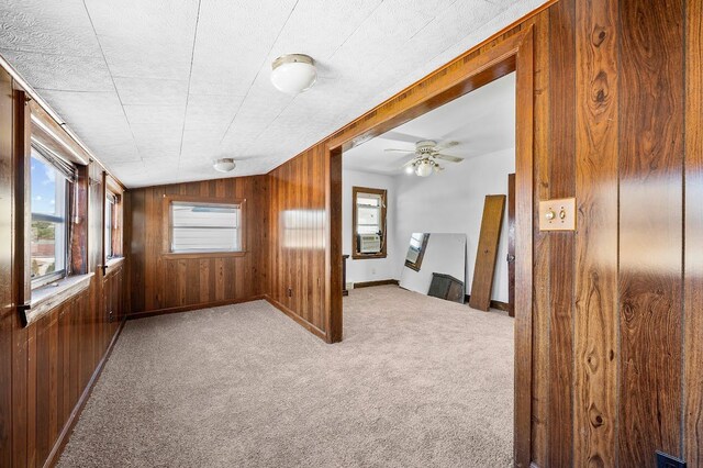 carpeted spare room featuring a ceiling fan, baseboards, wood walls, and plenty of natural light