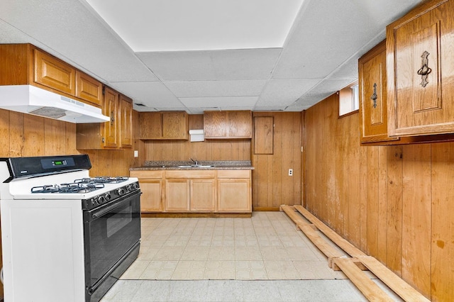 kitchen with range with gas stovetop, a sink, under cabinet range hood, wooden walls, and light floors