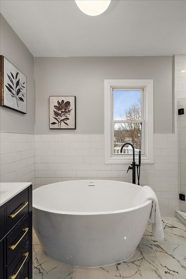 full bathroom featuring a freestanding bath, marble finish floor, and tile walls