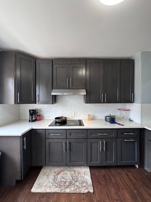 kitchen with light countertops, black electric stovetop, under cabinet range hood, decorative backsplash, and dark wood-type flooring