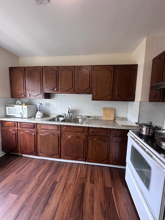 kitchen featuring white appliances, under cabinet range hood, dark wood finished floors, decorative backsplash, and a sink
