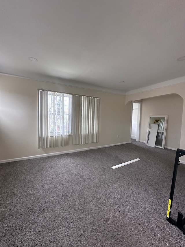 carpeted empty room with arched walkways and baseboards