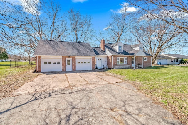 new england style home featuring a chimney, brick siding, aphalt driveway, a front lawn, and a garage
