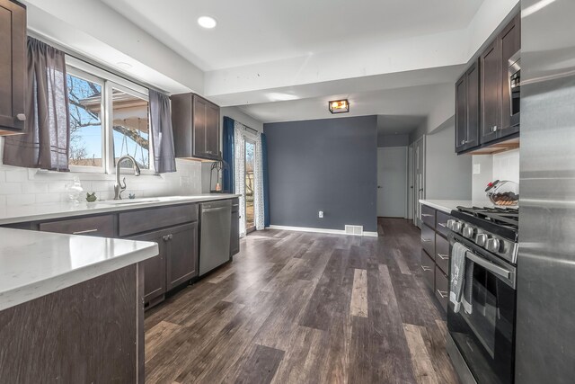 kitchen with decorative backsplash, visible vents, stainless steel appliances, a sink, and dark wood-style floors