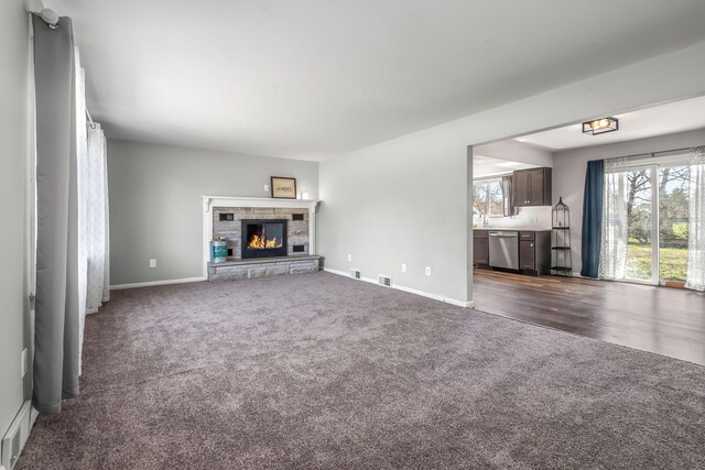 unfurnished living room with a stone fireplace, baseboards, visible vents, and dark colored carpet