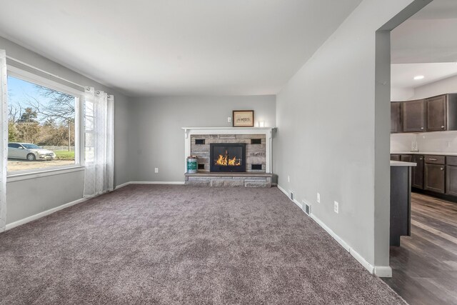 unfurnished living room with a stone fireplace, baseboards, visible vents, and dark colored carpet