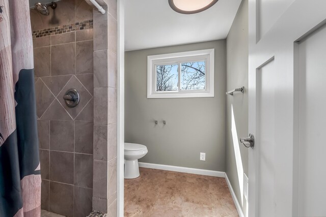 bathroom with toilet, baseboards, and a tile shower