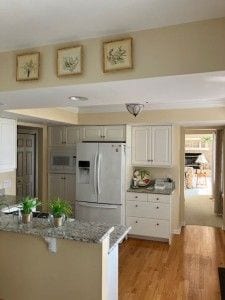kitchen with a kitchen breakfast bar, white fridge with ice dispenser, light wood finished floors, stone counters, and a peninsula