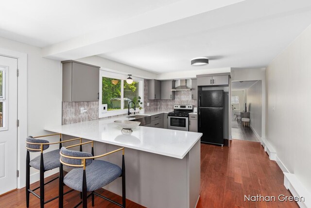 kitchen with electric stove, wall chimney range hood, gray cabinets, and freestanding refrigerator