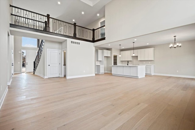 24599 Brookshire Dr, Macomb, MI 48042 - unfurnished living room featuring visible vents, a towering ceiling, baseboards, light wood-style flooring, and a notable chandelier
