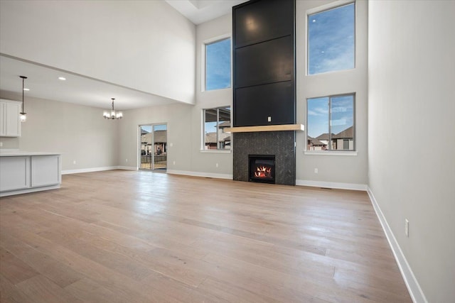 24599 Brookshire Dr, Macomb, MI 48042 - unfurnished living room with an inviting chandelier, a fireplace, baseboards, light wood-type flooring, and a towering ceiling