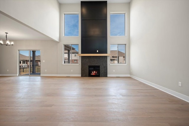 24599 Brookshire Dr, Macomb, MI 48042 - unfurnished living room with light wood-type flooring, a warm lit fireplace, a towering ceiling, and a notable chandelier