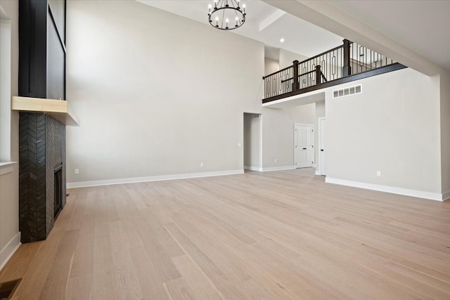 24599 Brookshire Dr, Macomb, MI 48042 - unfurnished living room featuring visible vents, a towering ceiling, a fireplace, light wood-style flooring, and a notable chandelier