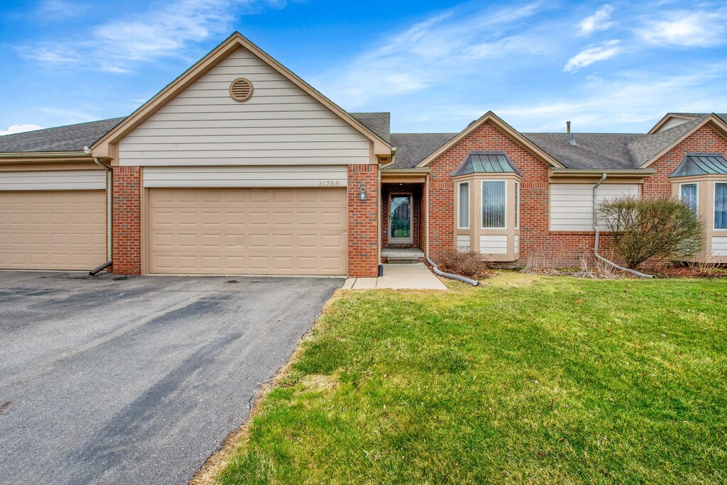single story home with a front yard, an attached garage, brick siding, and aphalt driveway