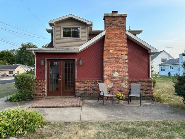 back of property featuring french doors, a chimney, brick siding, and a patio area