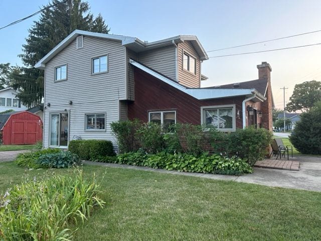view of side of property with a chimney, an outbuilding, a patio, a yard, and a storage shed