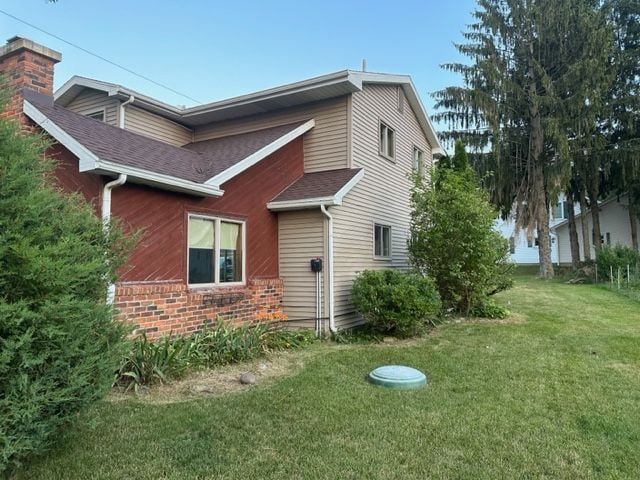 view of side of home featuring a shingled roof and a yard