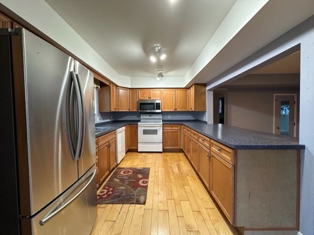 kitchen with a peninsula, light wood finished floors, stainless steel appliances, dark countertops, and brown cabinetry