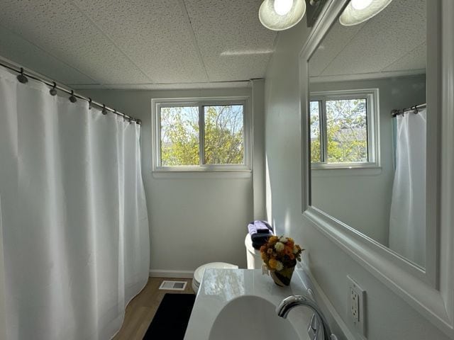 bathroom featuring visible vents, toilet, wood finished floors, a sink, and a paneled ceiling