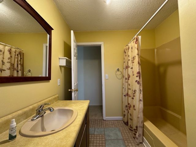 full bathroom featuring shower / bath combo, a textured ceiling, baseboards, vanity, and tile patterned flooring