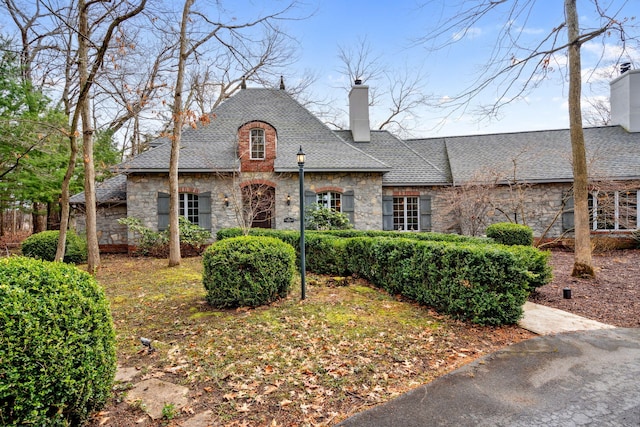 6242 131st St, Saugatuck, MI 49453 - french country inspired facade with stone siding, a chimney, and roof with shingles