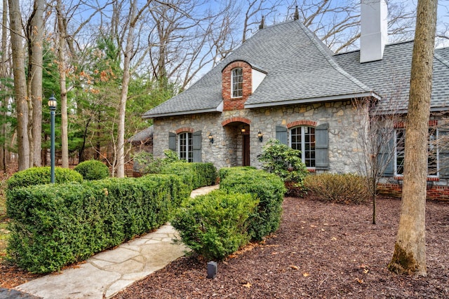 6242 131st St, Saugatuck, MI 49453 - french country home with a chimney, stone siding, and roof with shingles