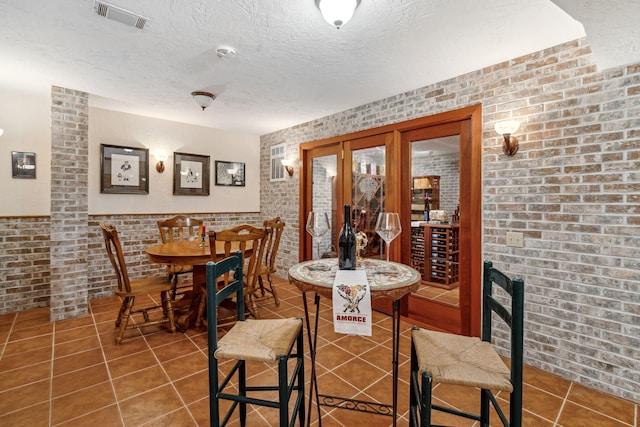 6242 131st St, Saugatuck, MI 49453 - dining space featuring tile patterned floors, a textured ceiling, wainscoting, brick wall, and visible vents