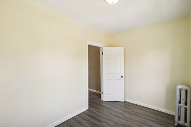 unfurnished room featuring radiator, baseboards, and dark wood-type flooring