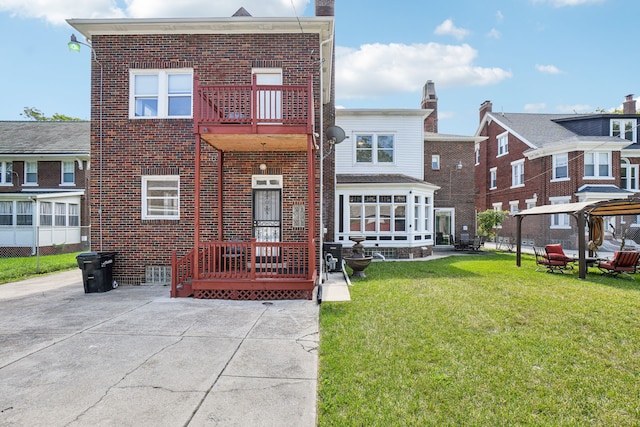 rear view of property featuring brick siding, a lawn, a patio, and a balcony
