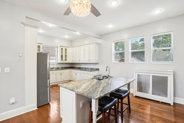 kitchen with a sink, freestanding refrigerator, wood finished floors, a ceiling fan, and a breakfast bar area