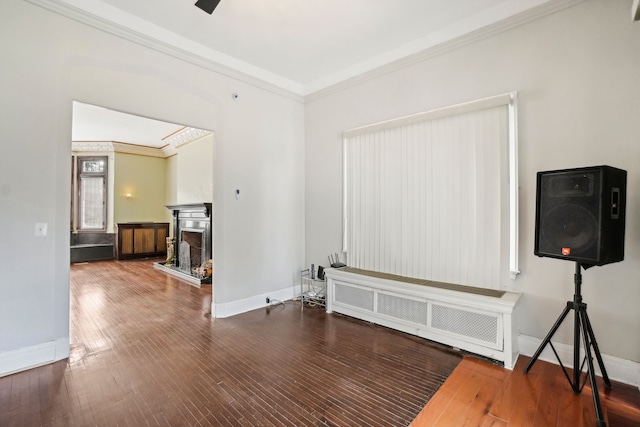 unfurnished living room featuring crown molding, baseboards, wood-type flooring, radiator, and a fireplace with raised hearth