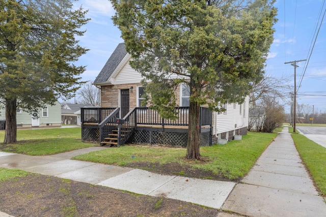 view of front of home with stone siding, roof with shingles, a front yard, and a deck